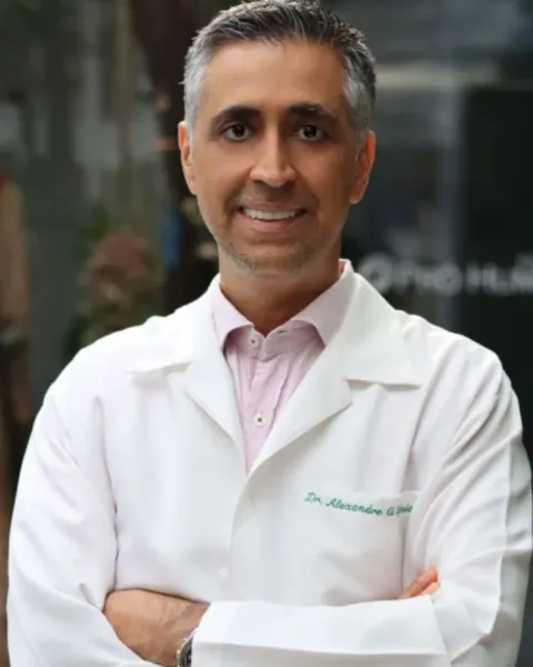 Dr. Alexandre Iglesia de jaleco, sorrindo, com os braços cruzados