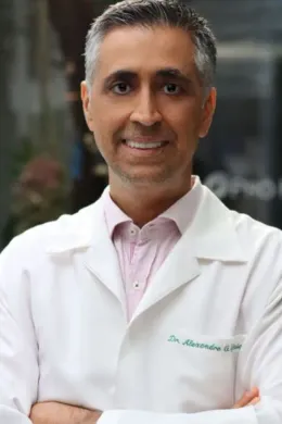 Dr. Alexandre Iglesia de jaleco, sorrindo, com os braços cruzados
